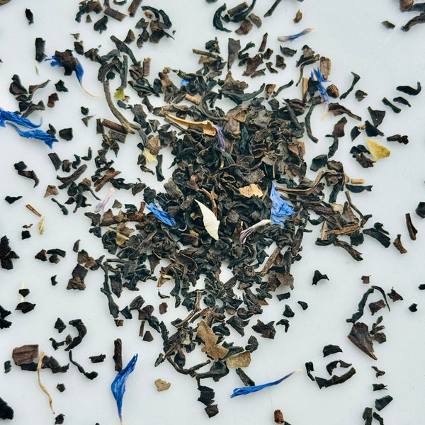 Loose leaf black tea leaves with cornflower blue flowers on a white background